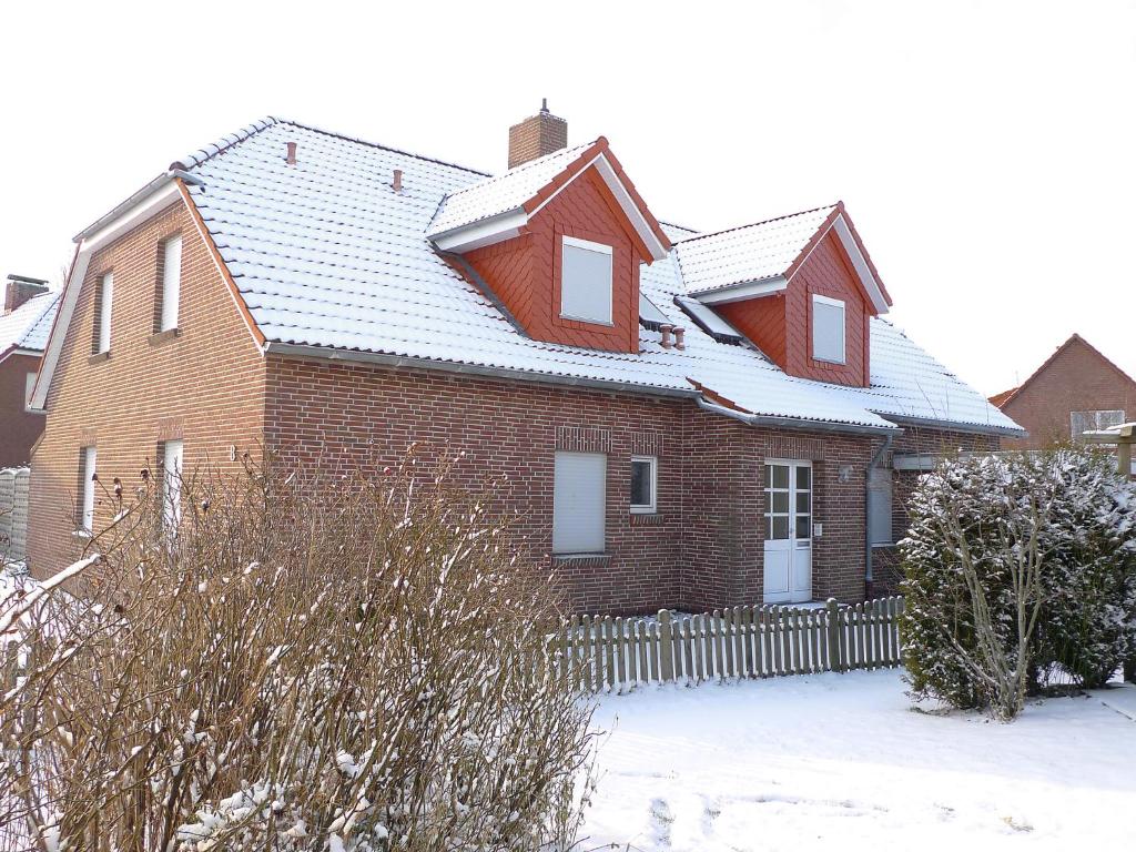 ein rotes Backsteinhaus mit einem Zaun im Schnee in der Unterkunft Apartment Tjalkstrasse-2 by Interhome in Norddeich