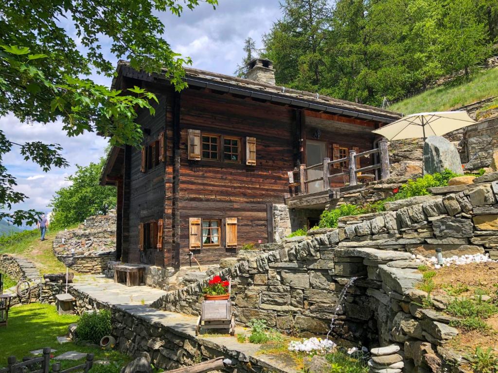 a log cabin with a stone wall and an umbrella at Chalet Bildji by Interhome in Staldenried