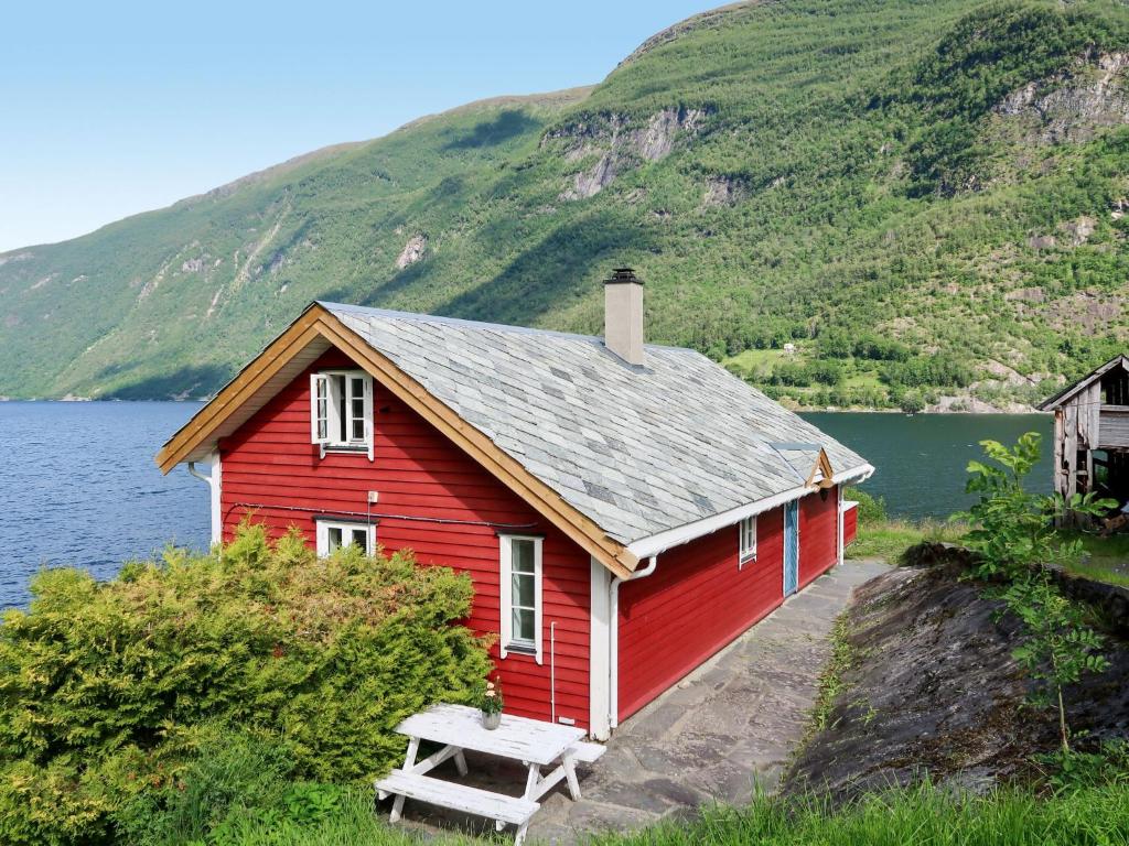 una casa roja con un banco frente a un lago en Holiday Home Johans Maria stova - FJS606 by Interhome, en Arnefjord