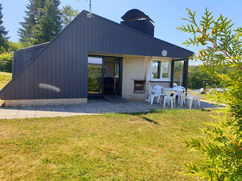 una casa con techo negro y mesas y sillas blancas en Holiday Home Waldferienpark Gerolstein-12 by Interhome, en Gerolstein