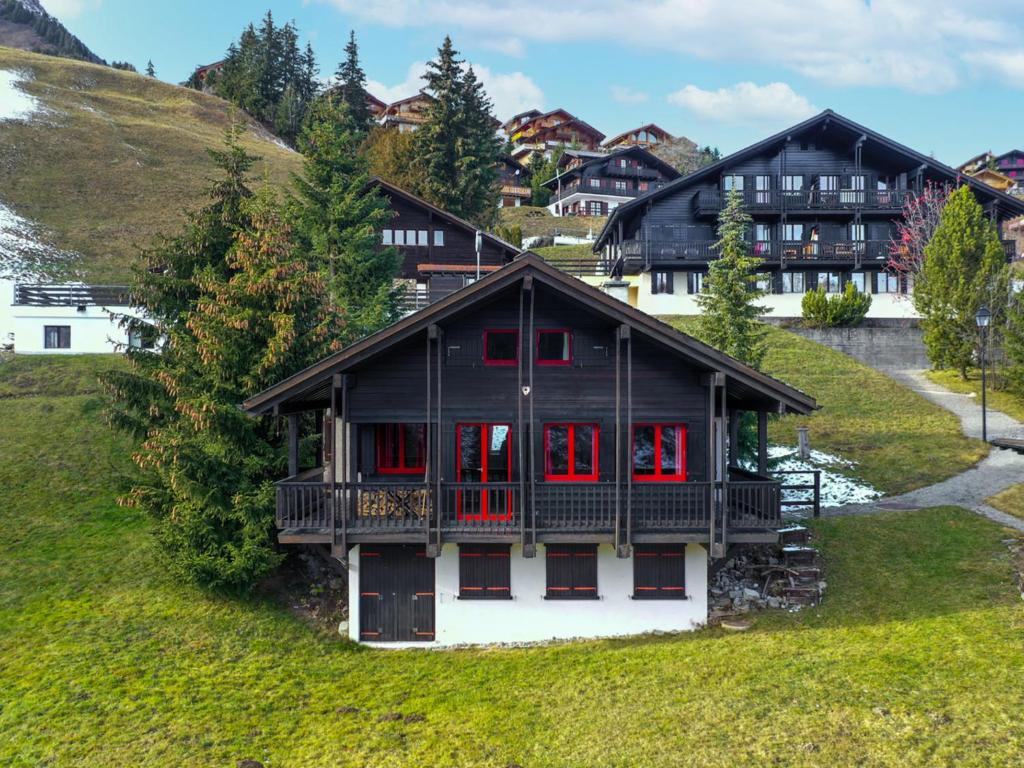 a black house with red windows on a hill at Chalet Le Cyclamen by Interhome in Champoussin