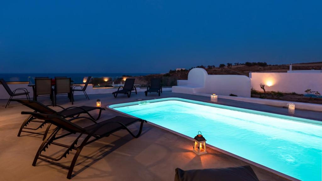 einen Pool in der Nacht mit Stühlen und einem Tisch in der Unterkunft Villa Waves in Monolithos