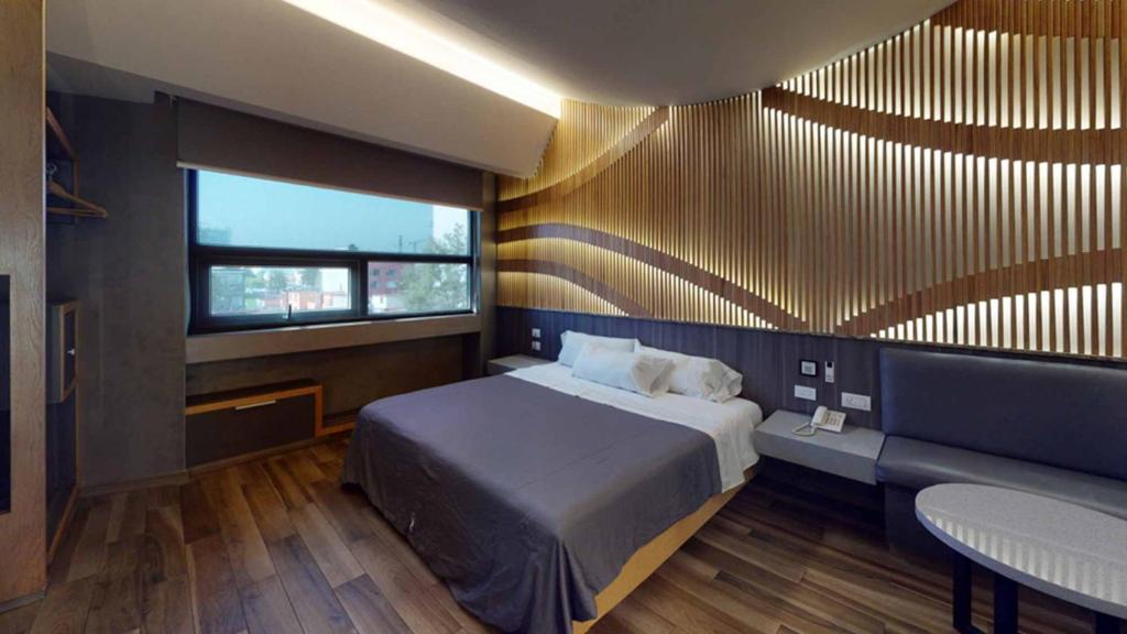 Schlafzimmer mit einem Bett, einer Bank und einem Fenster in der Unterkunft Hotel Patriotismo in Mexiko-Stadt