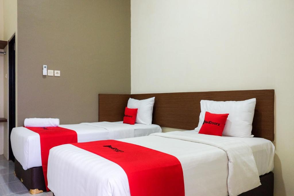 - 2 lits dans une chambre avec des draps rouges et blancs dans l'établissement RedDoorz Syariah near Exit Tol Pemalang Comal 2, à Comal