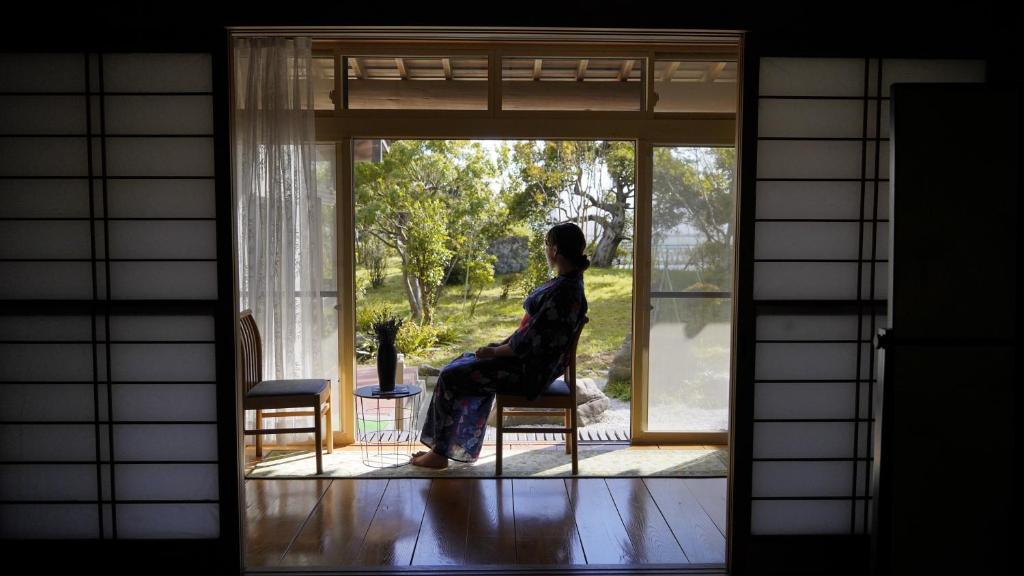 Una donna seduta su una sedia che guarda fuori da una porta di みんなの実家門脇家 ad Akita