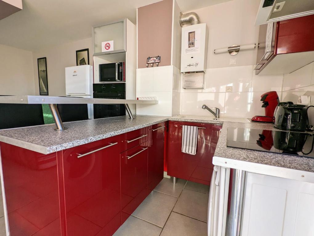 a kitchen with red cabinets and a microwave at Appartement cosy avec parking proche port et plage in Cap d&#39;Agde