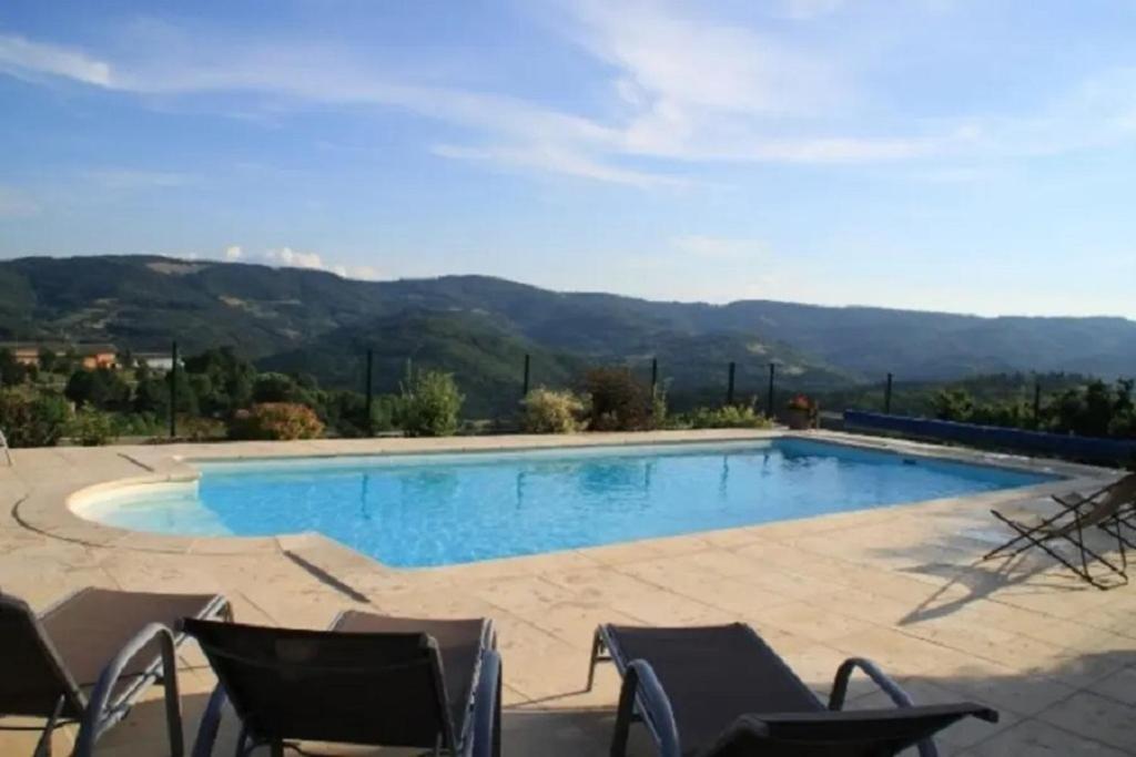 a swimming pool with chairs and mountains in the background at Gîtes Le Triskèle in Rochepaule