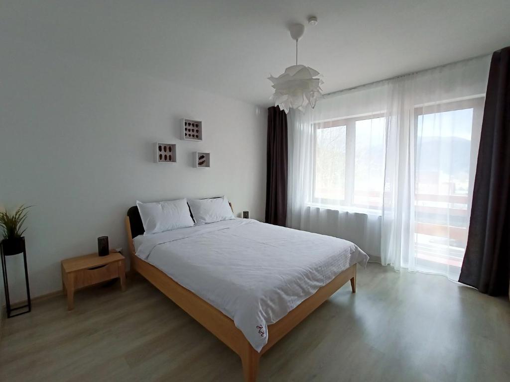 a white bedroom with a bed and a large window at Zander Home Apartment in Buşteni