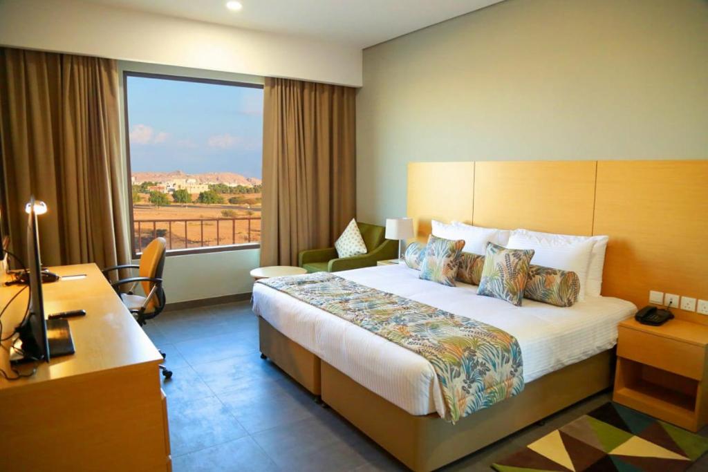 a hotel room with a bed and a large window at Ayla Ibri Hotel in ‘Ibrī