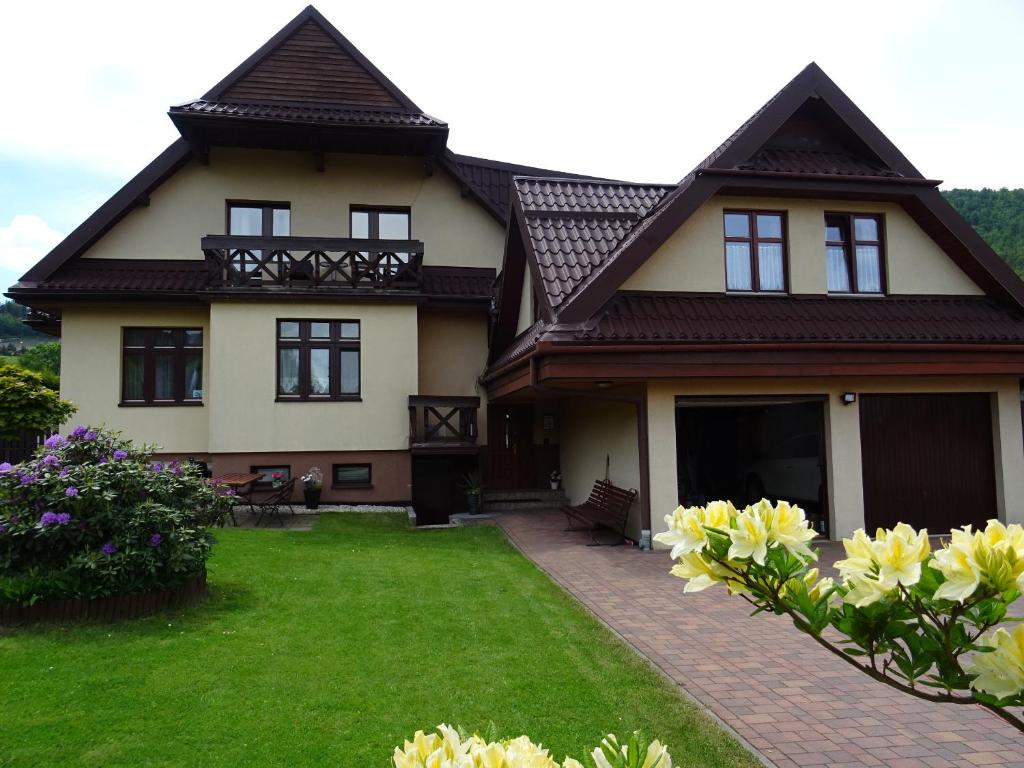 a house with a green yard with yellow flowers at Olimp pokoje i apartamenty in Szczyrk