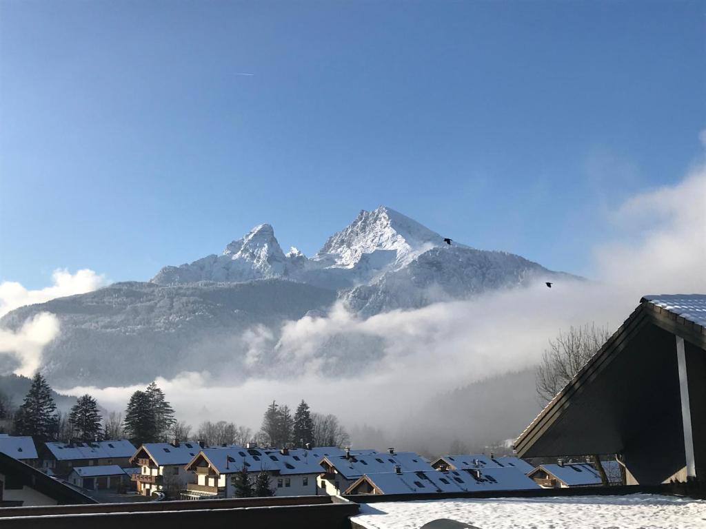 a snow covered mountain in the distance with a town and clouds at Ferienwohnung Watzmannblick & Hallenbad in Berchtesgaden