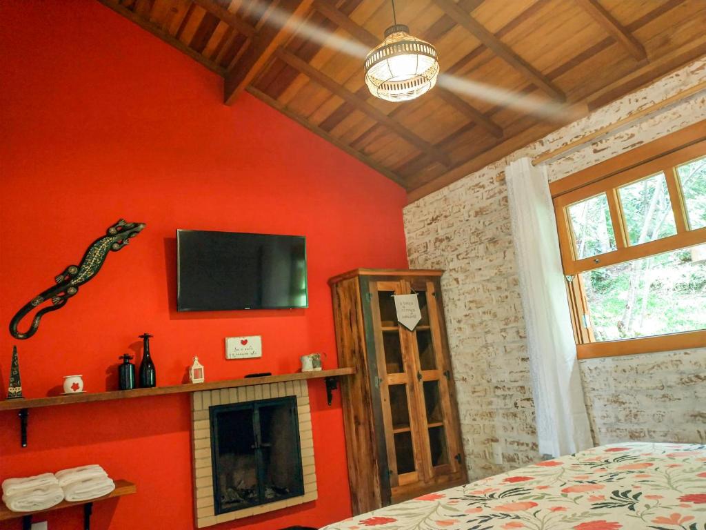 una camera da letto con una parete rossa, una TV e un camino di Nas Nuvens Hospedaria a Monte Verde