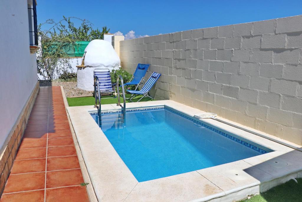 a swimming pool with two chairs next to a wall at Chalet Chaparrillo in Conil de la Frontera