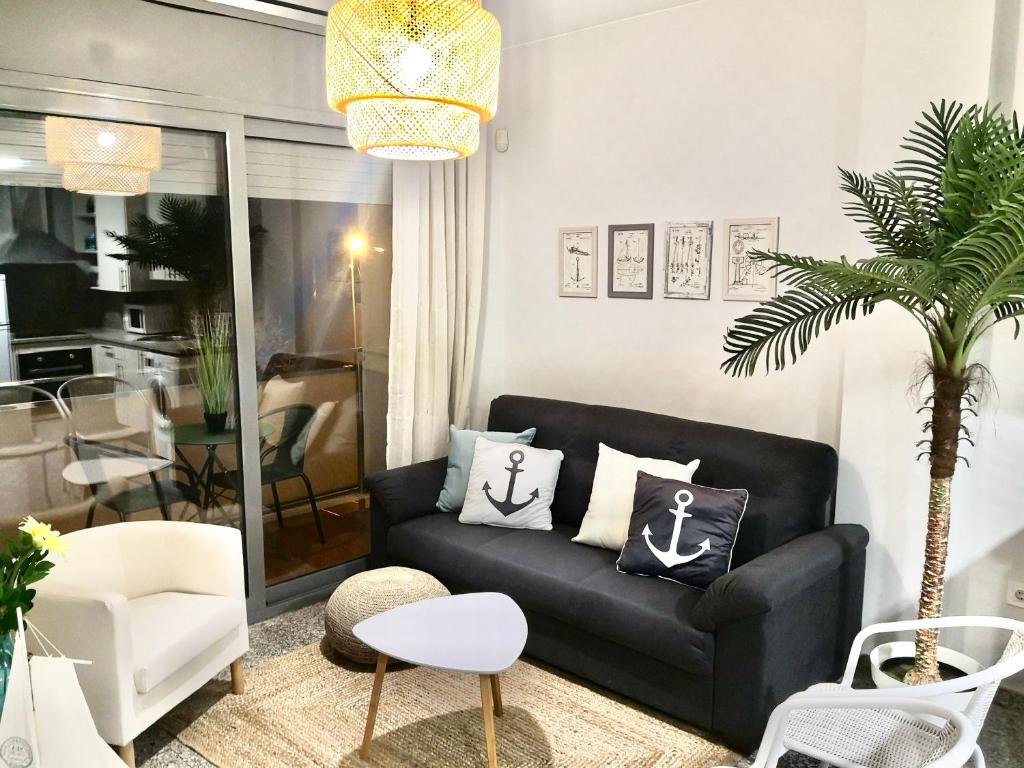 a living room with a black couch and a palm tree at SeaHomes Vacations, BEACH&POOL, in Fenals Beach in Lloret de Mar
