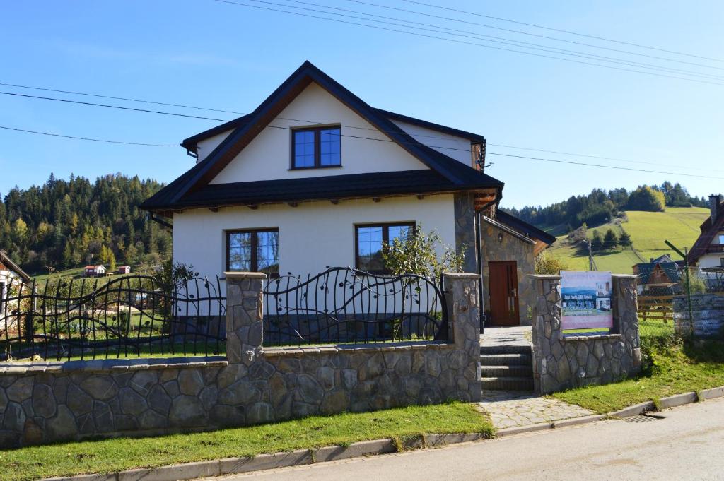 a small white house with a stone fence at Domek pod Majową Górą in Kacwin