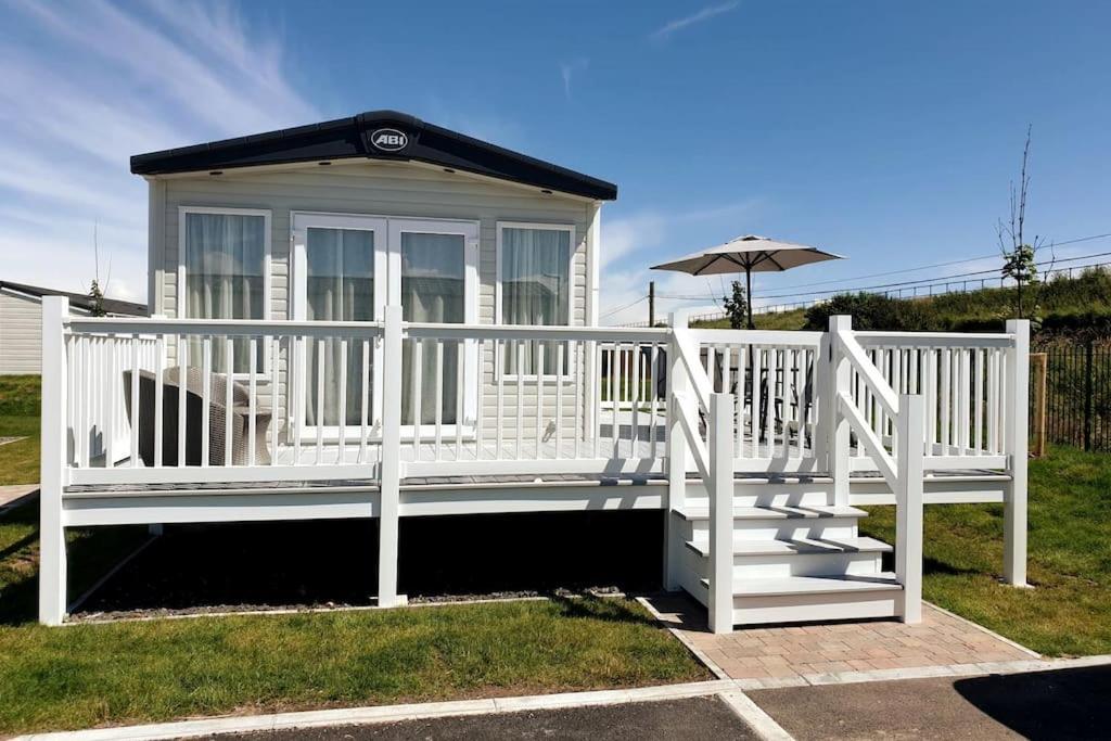 ein kleines weißes Haus mit einem Regenschirm und einer Treppe in der Unterkunft The Sea Breeze - 8 Berth Premium Caravan in Camber Sands in Camber