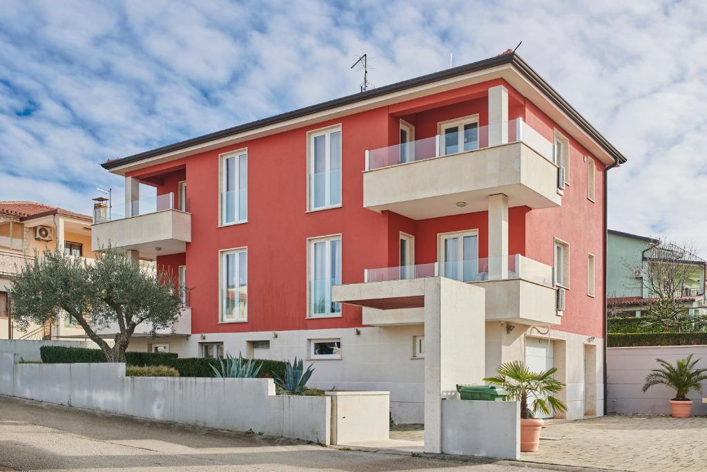 ein rotes Gebäude mit weißen Balkonen auf einer Straße in der Unterkunft VILLA AX in Umag