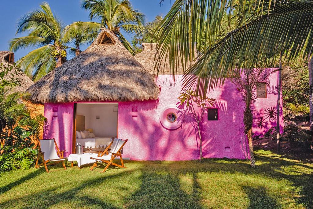 uma casa cor-de-rosa com duas cadeiras à frente. em Bungalows & Casitas de las Flores in Careyes em Careyes