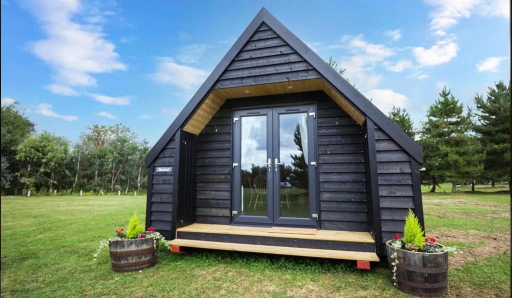 ein schwarzes winziges Haus mit einem Fenster auf einem Feld in der Unterkunft Wildflower Meadow Cabins in Whitington