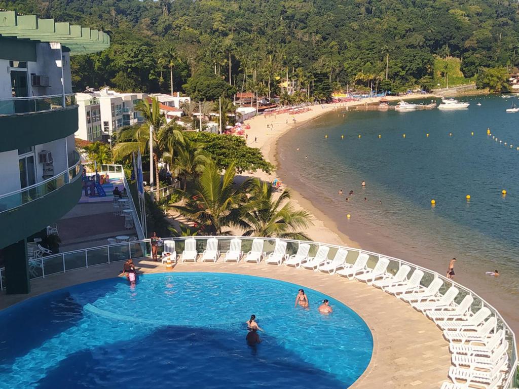 a swimming pool next to a beach with people in the water at Angra Praia Grande Flat Studio Angra Inn - O Mar de Angra te espera ! in Angra dos Reis
