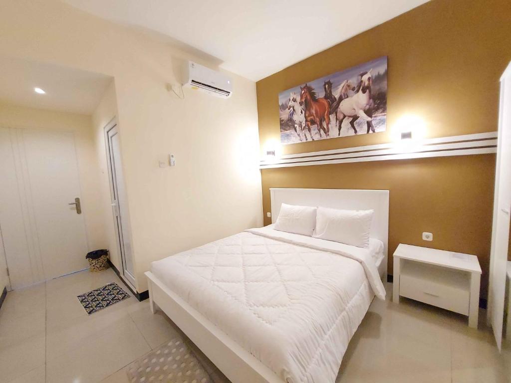 Un dormitorio con una cama blanca y una pintura en la pared en Rons City Hotel near Simpang Lima Semarang Mitra RedDoorz en Semarang