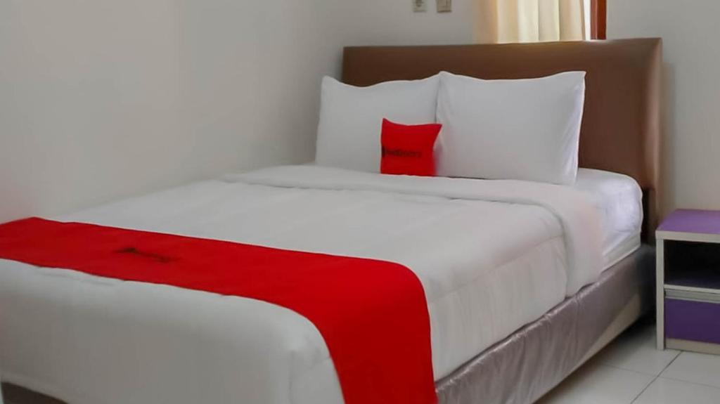 1 dormitorio con cama blanca y almohada roja en RedDoorz @ Jalan Ahmad Yani, en Karawang
