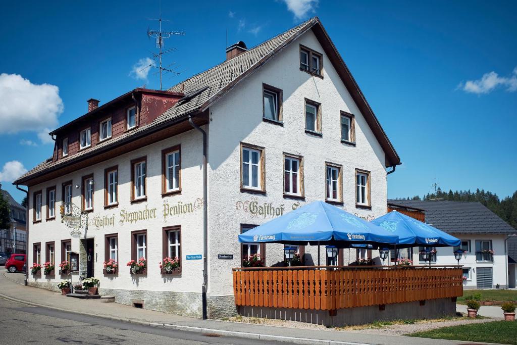 ein weißes Gebäude mit blauen Sonnenschirmen davor in der Unterkunft Gasthof & Pension Steppacher in Friedenweiler