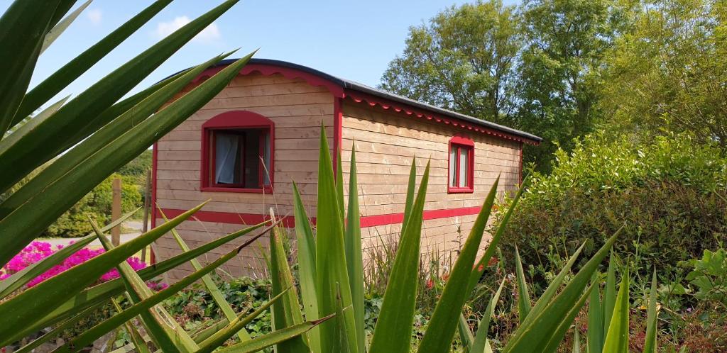 une petite maison avec des fenêtres rouges dans un jardin dans l'établissement LE PETIT NID DANS LA ROULOTTE, à Roscanvel