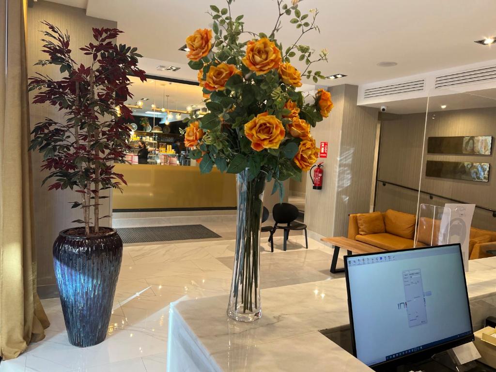 a vase with orange flowers and a laptop on a table at Hotel Avenida Gran Vía in Madrid