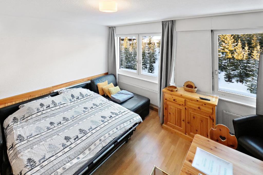 a bedroom with a bed and a chair and two windows at Studio cosy au centre de Crans-Montana (1-4 personnes) in Crans-Montana
