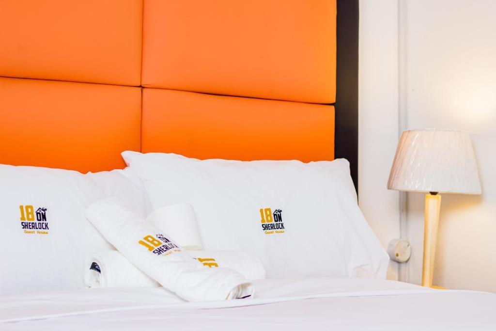 uma cama com almofadas brancas e uma cabeceira laranja em 18 on sherlock em Port Elizabeth