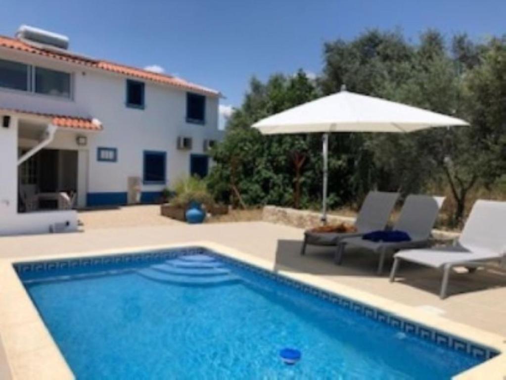 a swimming pool with an umbrella and chairs and a house at vivenda descollaz in Falcoeiras