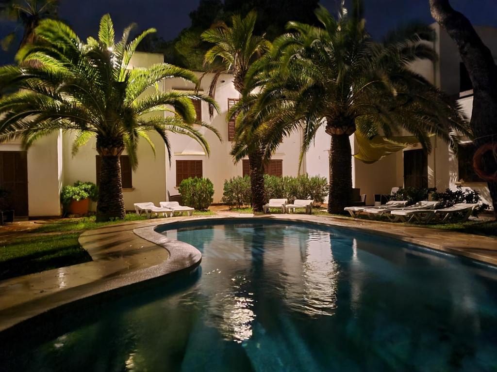 a swimming pool with palm trees in front of a building at Apartamentos Osa Menor in Cala d´Or