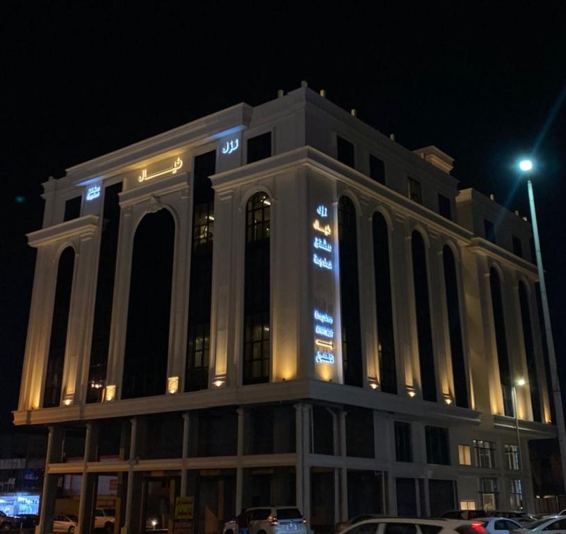 Un grand bâtiment blanc avec des lumières allumées la nuit dans l'établissement نزل خيال للشقق المخدومه, à Jazan