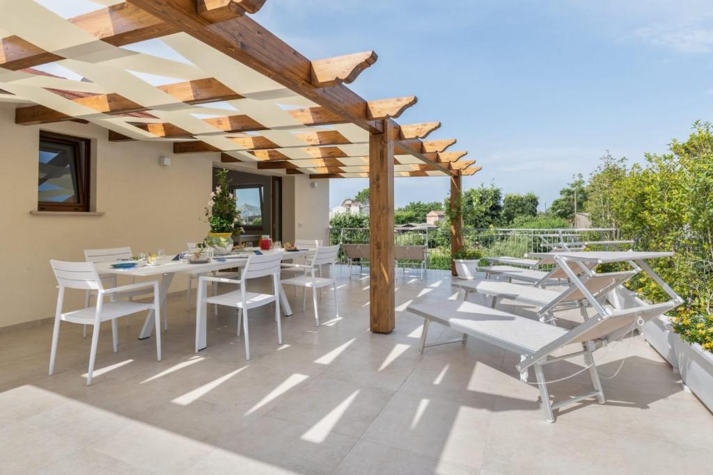 un patio con mesas blancas y sillas bajo una pérgola de madera en LeMoon Holiday Home x7 con Terrazzo e Parcheggio, en Massa Lubrense