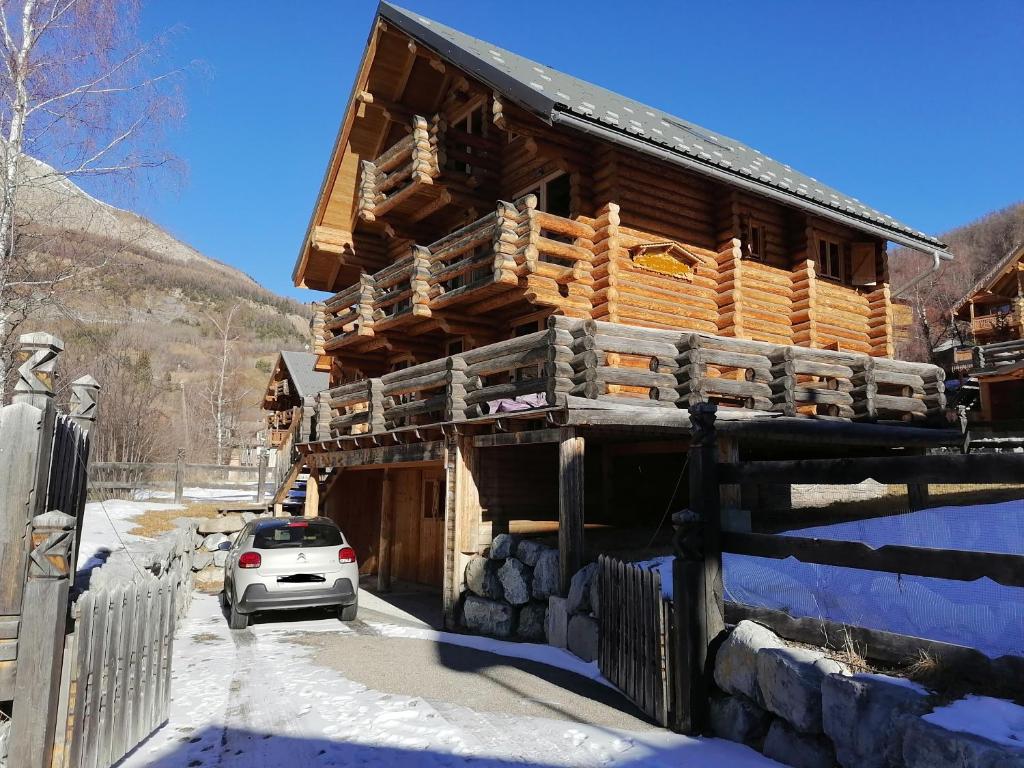 una baita di tronchi nella neve con un'auto parcheggiata fuori di Chalet Les Pins Blancs ad Allos