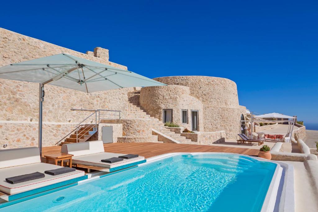 a swimming pool with two chairs and an umbrella at Kamini Santorini Villas in Pyrgos