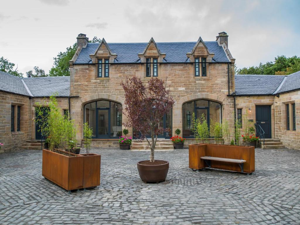 een groot bakstenen gebouw met bomen ervoor bij Coach House Ratho Park Steading in Ratho