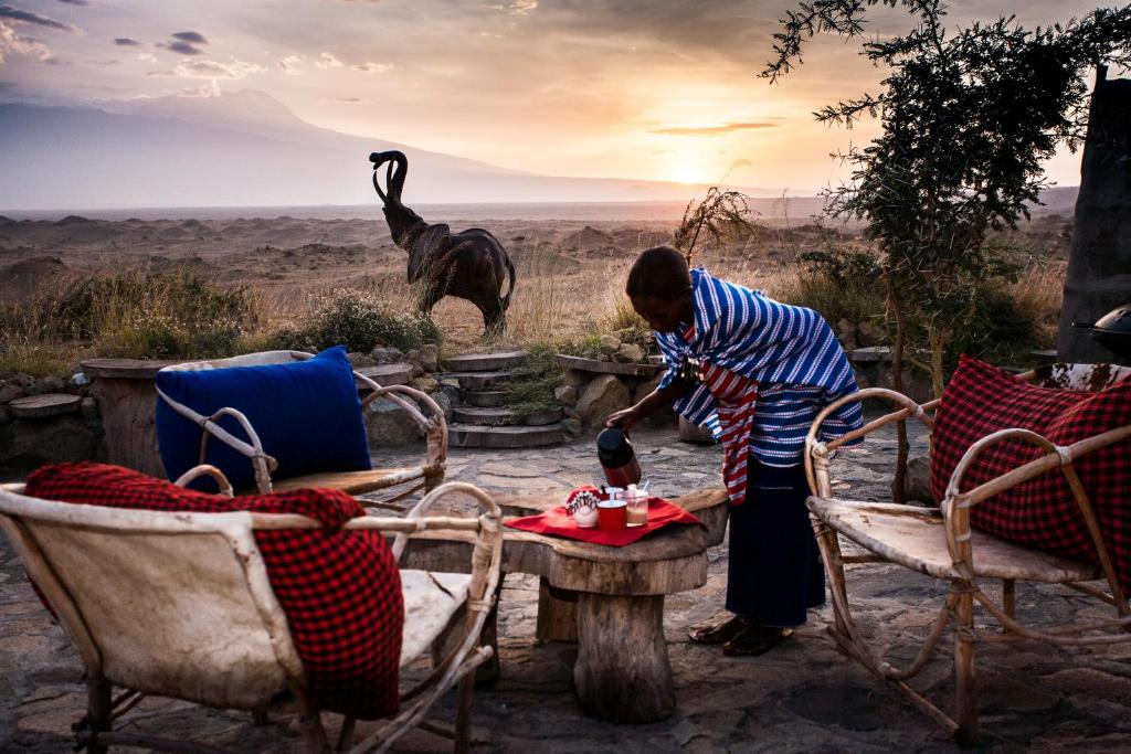 a woman standing in front of a table with an elephant in the background at Original Maasai Lodge – Africa Amini Life in Ngare Nanyuki