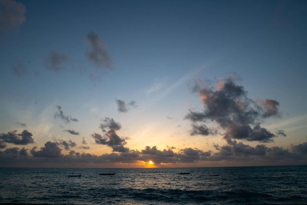 a sunset over the ocean with clouds in the sky at Nur Beach Hotel in Jambiani