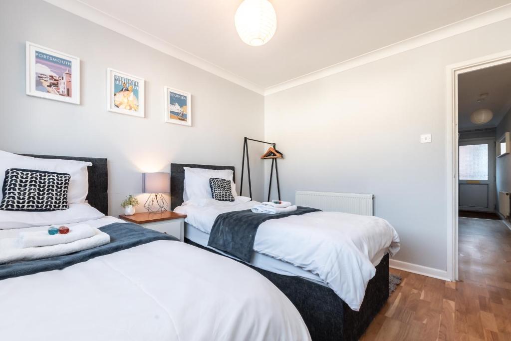 two beds in a bedroom with white walls and wood floors at BEST PRICE! - 1 MIN TO THE SHOPS, BARS, PUBS & RESTAURANTS! PERFECT LOCATION - FREE PARKING - FREE WIFI - SMART TV - COMFY BEDS - 4 Single beds or 2 Doubles in Portsmouth
