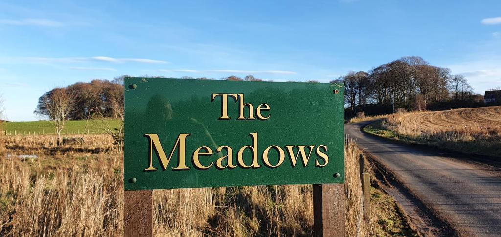 a green sign that reads the meadows on a road at Spacious well equipped Chalet Bungalow close to Nairn, in Auldearn