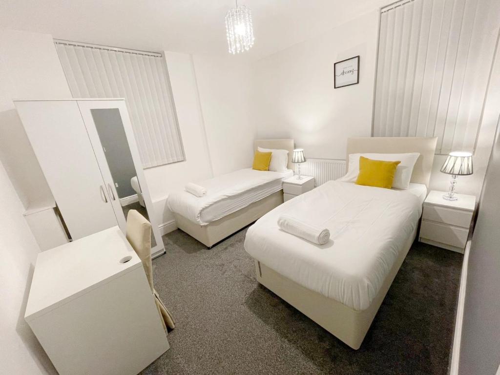 a white bedroom with two beds and a mirror at New Brighton Flat in Wallasey