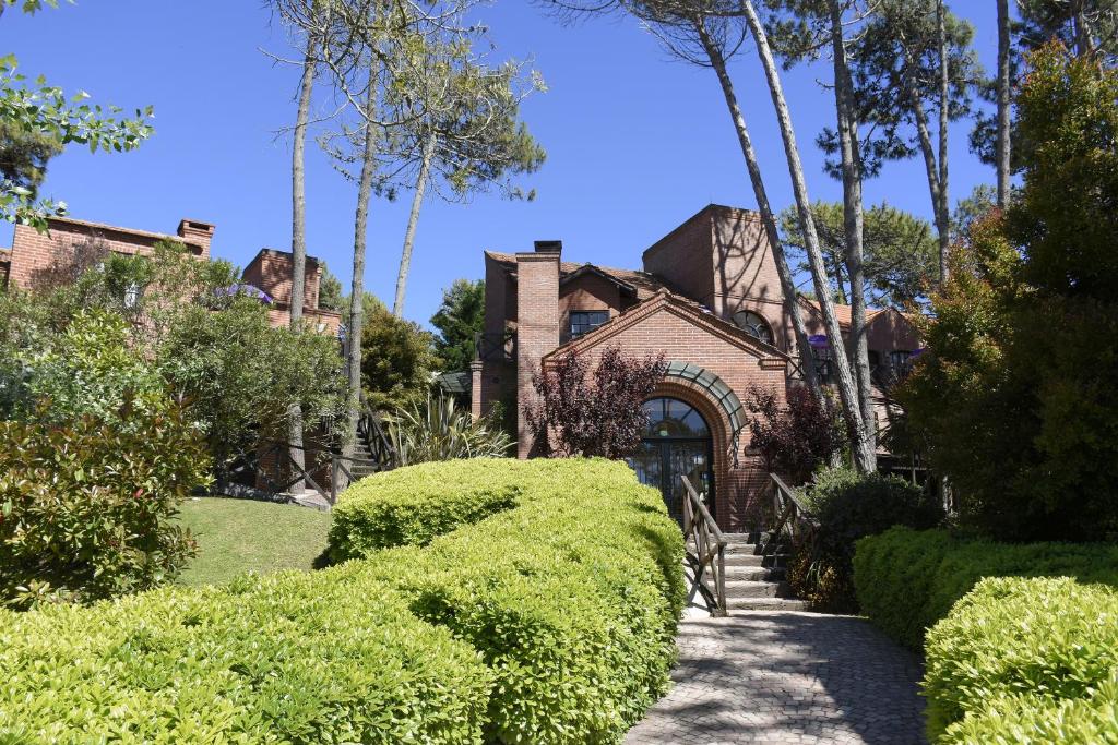 uma casa de tijolos com sebes à frente em Apart Hotel Las Hadas Carilo em Carilo