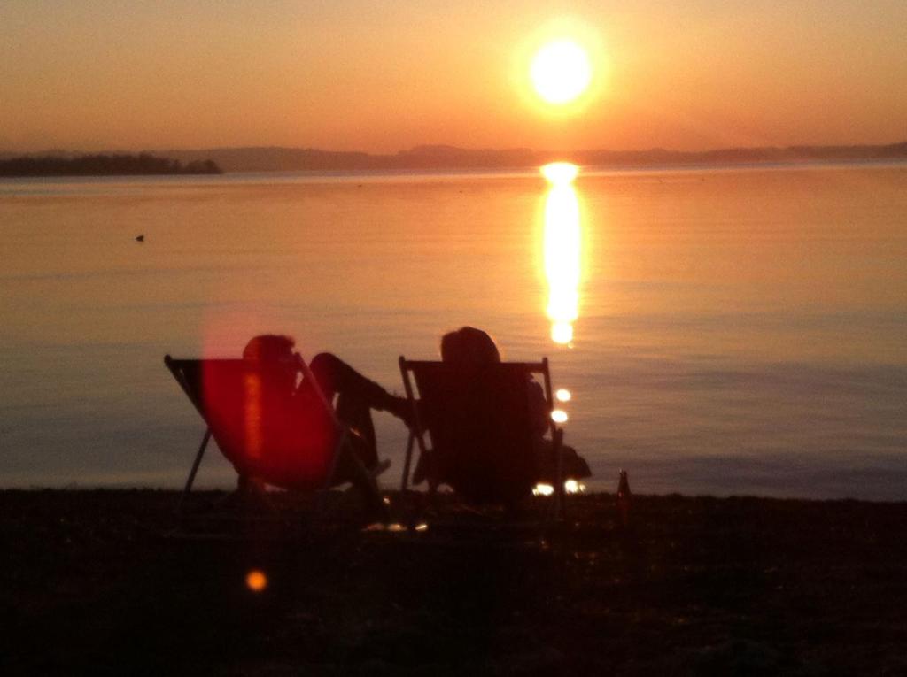 two people sitting in chairs on the beach watching the sunset at Genusszeit am Chiemsee in Übersee