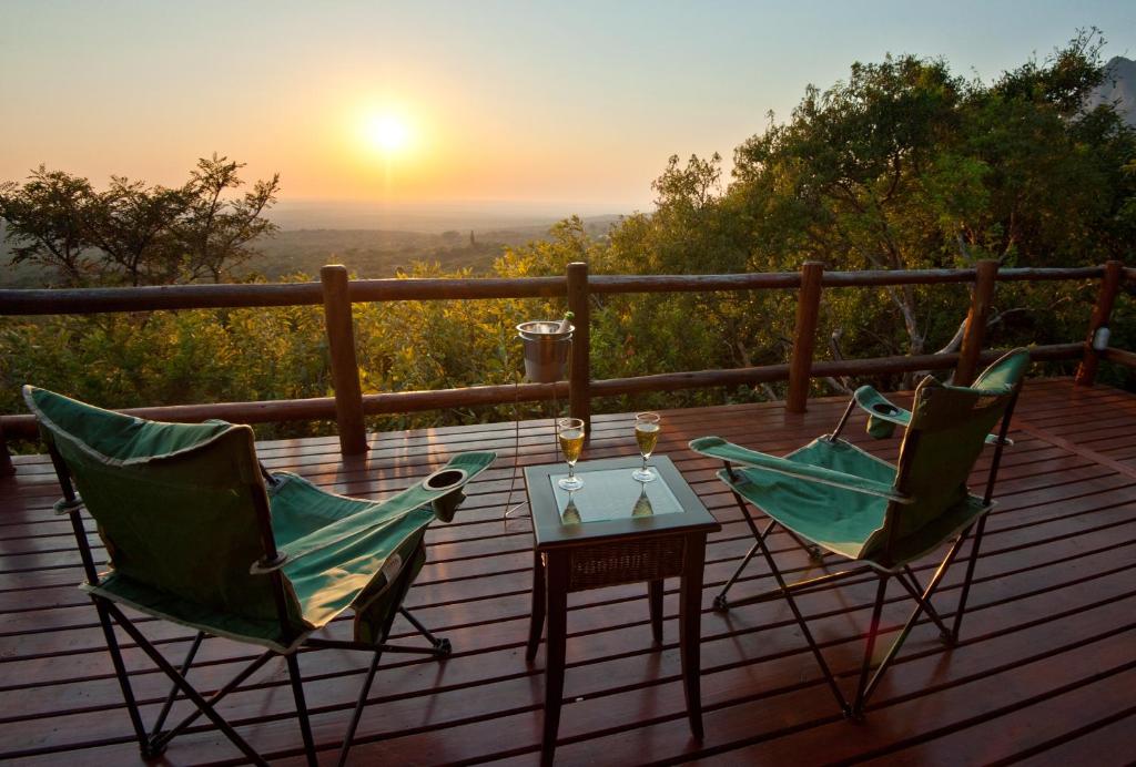 two chairs and a table on a deck with the sunset at Amafu Forest Lodge in Hoedspruit