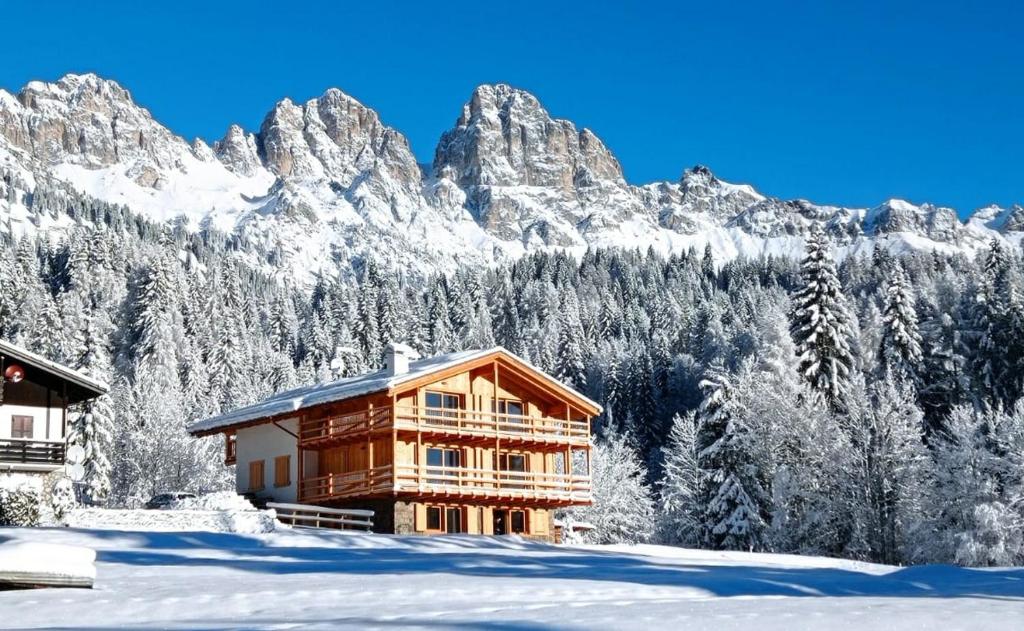 a house in the snow with mountains in the background at Tabiá sui Prá - appartamento monolocale Anna in Falcade