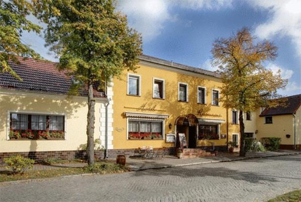 ein großes gelbes Gebäude mit einem Baum davor in der Unterkunft Hotel-Restaurant Alter Krug Kallinchen in Kallinchen