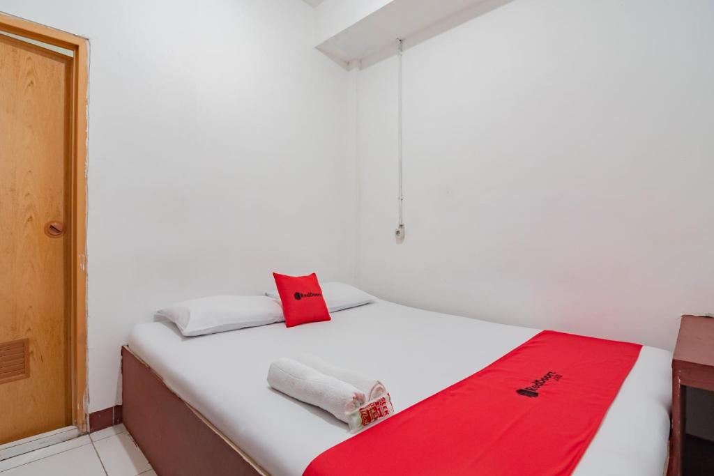 a bedroom with a white bed with a red blanket on it at RedDoorz near Riau Junction Mall 2 in Bandung