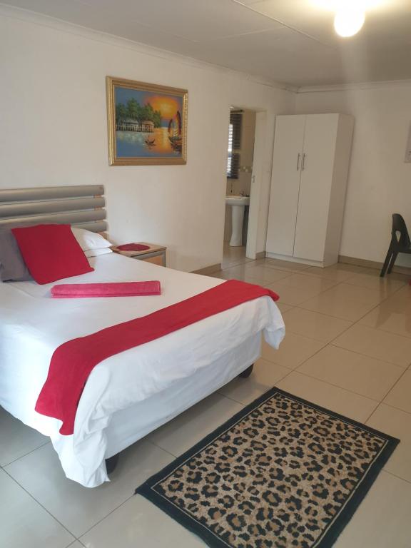 a bedroom with a large white bed with red sheets and a rug at Rose Guesthouse Klerksdorp in Klerksdorp